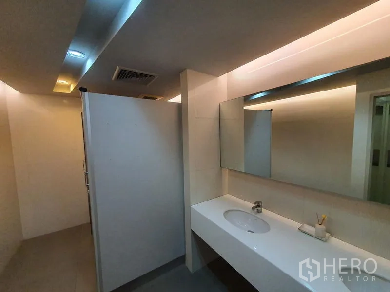 Office Space for rent in Watthana, Bangkok - Modern office restroom with a long white vanity, mirror, and partitioned stalls.