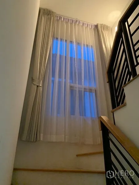 Detached House for sale in Prawet, Bangkok - Staircase with black railings and a tall window with sheer curtains.