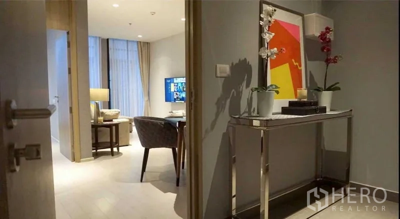 Condominium for rent in Pathum Wan, Bangkok - Entry hallway with console table, orchids and colorful wall art leading to living room.