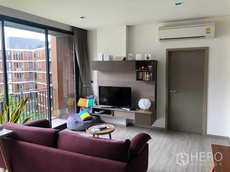 คอนโด ให้เช่าในWatthana, Bangkok - พื้นที่นั่งเล่นมีชั้นวางทีวีข้างระเบียง มองเห็นสวน