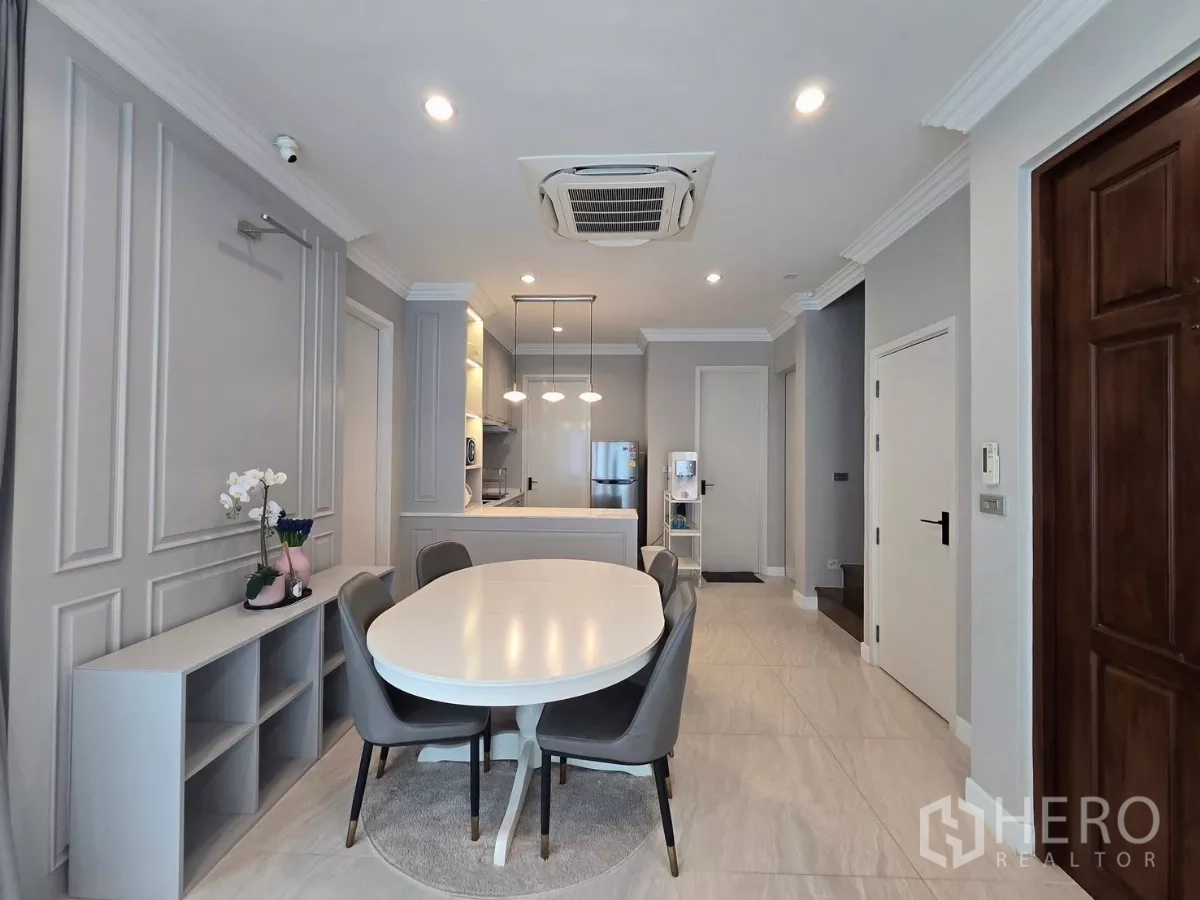 Detached House for rent in Prawet, Bangkok - Open‑plan dining area with oval table leading to a kitchen illuminated by pendant lights.