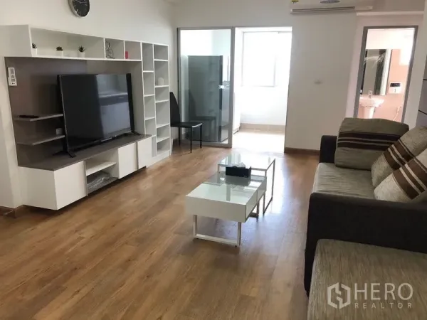 Condominium for rent in Huai Khwang, Bangkok - Living room with TV console and shelving, sliding door to laundry zone, and view toward bathroom entrance.