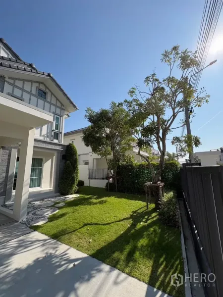 Detached House for rent in Bang Phli, Samut Prakan - Lawn and driveway beside the house with mature trees and neat landscaping.