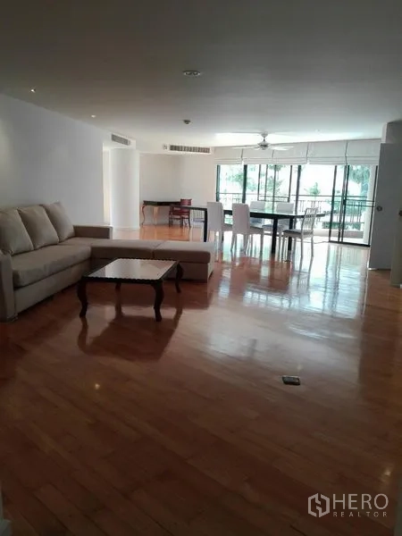 คอนโด ให้เช่าในKhlong Toei, Bangkok - ห้องนั่งเล่นแบบโอเพ่นสเปซ พื้นไม้เงางาม โซฟา โต๊ะกลาง และหน้าต่างสูงเปิดสู่ระเบียง