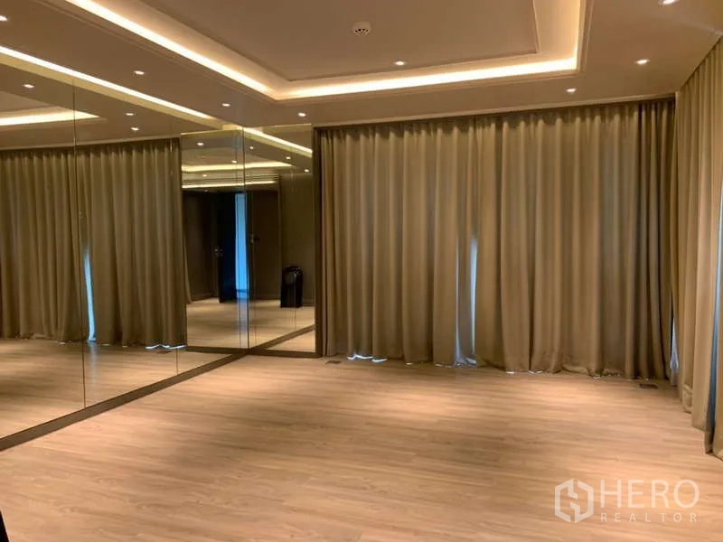 Condominium for rent in Khlong Toei, Bangkok - Multipurpose room with mirrored wall, recessed ceiling lights, wood flooring and full curtains.