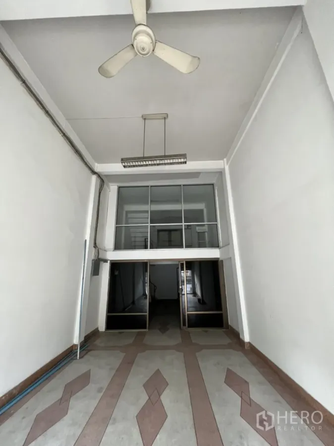 店屋 出租在Phra Khanong, Bangkok - 临街商铺一层，挑高空间，吊扇与几何地砖，前方玻璃夹层隔间。