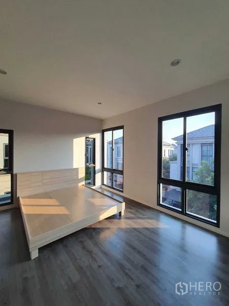 Detached House for sale in Prawet, Bangkok - Sunlit bedroom with large corner windows and wood flooring.