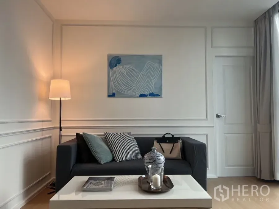 Condominium for rent or sale - Stylish living room with sofa, artwork, cushions and natural light from tall curtains.