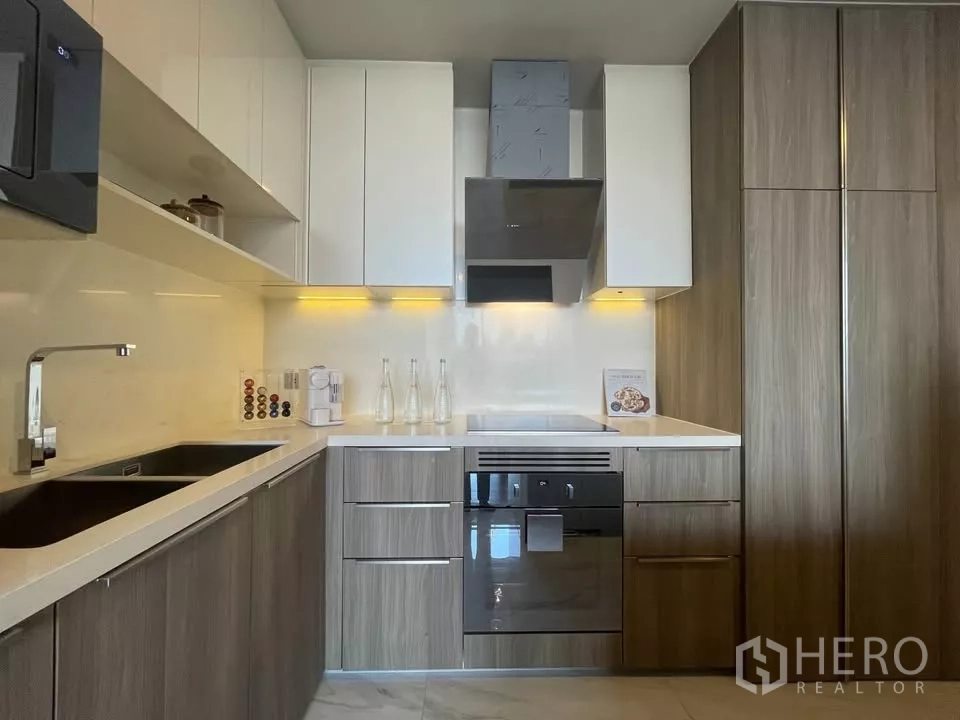 Condominium for rent in Watthana, Bangkok - Fully fitted L-shaped kitchen with wood cabinetry, built-in oven and range hood.