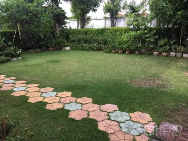 独立式住宅 出售在Bang Kruai, Nonthaburi - 宽阔草坪，四周灌木环绕并铺设彩色石道。