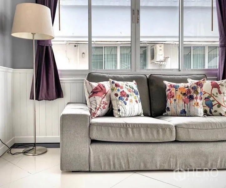 คอนโด ให้เช่าในKhlong Toei, Bangkok - โซฟาผ้าเทาพร้อมหมอนลายดอกไม้ ข้างหน้าต่างบานเลื่อนและโคมไฟตั้งพื้น