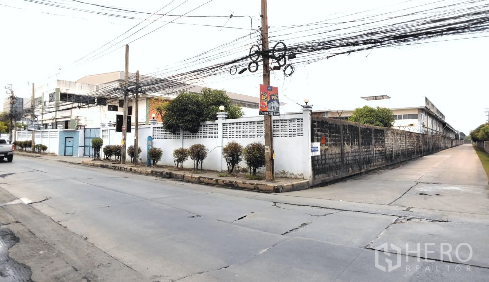 Factory for rent or sale in Bang Phli, Samut Prakan - Corner view of the walled compound along a public road with power lines.