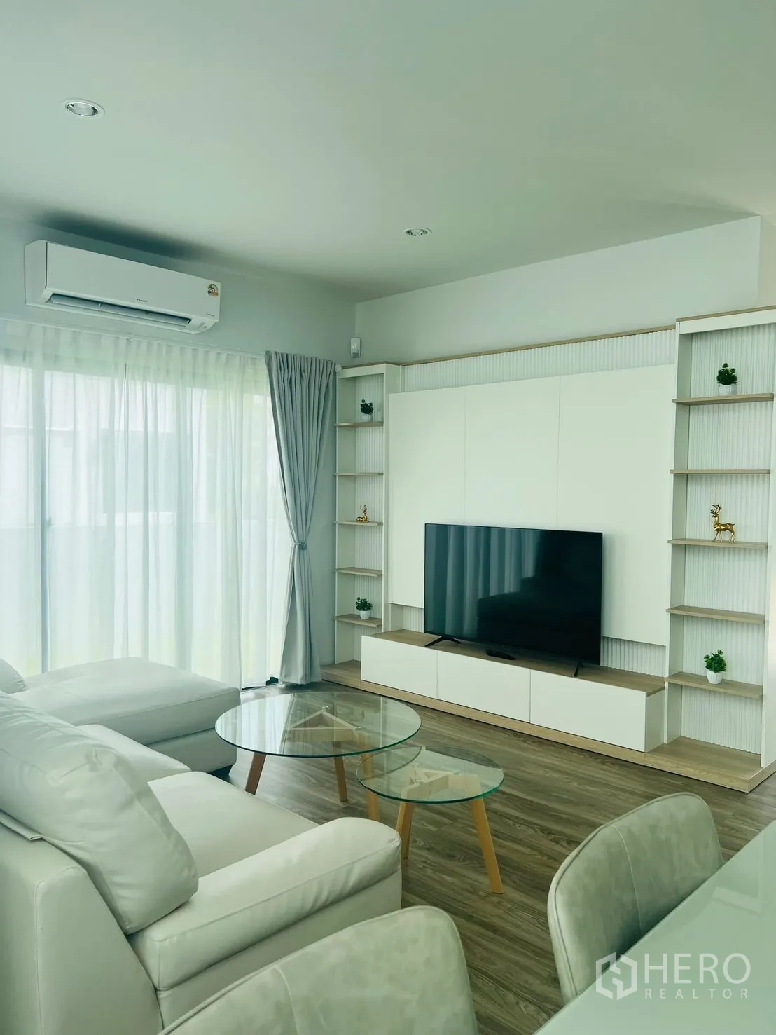 บ้าน ให้เช่าในBang Sao Thong, Samut Prakan - ห้องนั่งเล่นสว่าง โซฟาเข้ามุม โต๊ะกระจก ผนังบิลท์อินวางทีวี และผ้าม่านโปร่ง