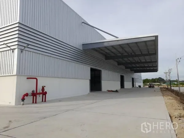 工厂 出租在Mueang Rayong, Rayong - 金属板外立面的现代工厂，带大雨棚装卸区、宽阔混凝土场地及红色消防管。