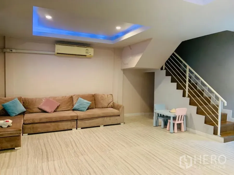 Detached House for sale in Din Daeng, Bangkok - Spacious living room with beige sofa, recessed blue LED ceiling and staircase.