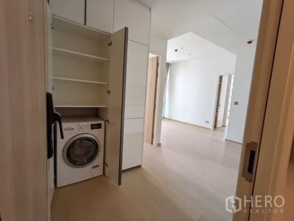Condominium for sale - Built-in utility cabinet with shelving and a front-load washer in a modern condo hallway.