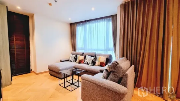 Condominium for sale in Watthana, Bangkok - Corner living room with L-shaped sofa, floor-to-ceiling window and sheer curtains for natural light.