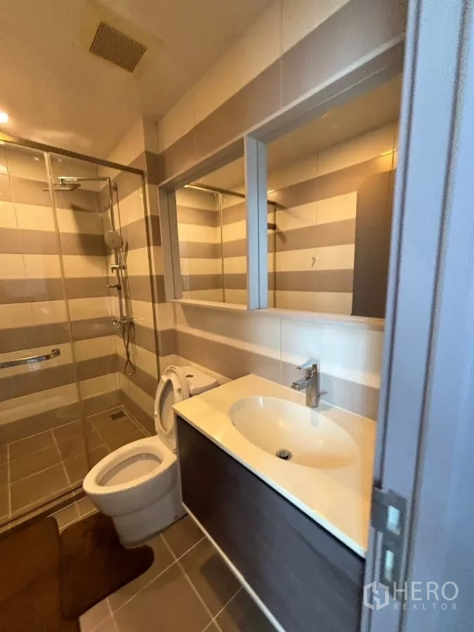 Condominium for rent or sale in Watthana, Bangkok - Bathroom vanity with large mirror beside a walk-in shower and toilet.