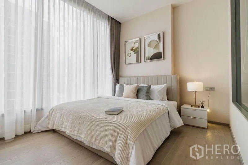 Condominium for rent in Watthana, Bangkok - Bright bedroom with a large bed, soft neutral tones, and full-height windows.