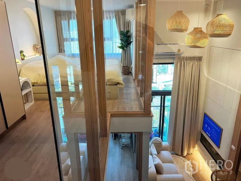 คอนโด ให้เช่าในHuai Khwang, Bangkok - ทางเดินกระจกเชื่อมห้องชั้นลอย มองเห็นห้องรับแขกเพดานสูง พร้อมทีวีและโคมหวาย