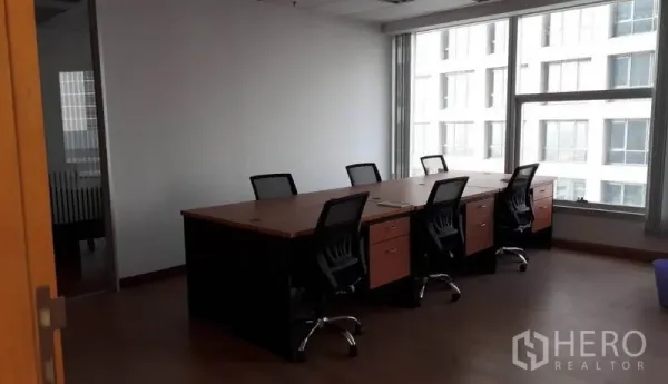 Office Space for rent in Bang Rak, Bangkok - Meeting area with a large shared desk and office chairs beside a wide window overlooking a neighboring building.