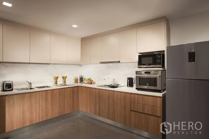 อพาร์ทเมนท์ ให้เช่าในKhlong Toei, Bangkok - ครัวรูปตัวแอลสมัยใหม่ ตู้ล่างลายไม้ ตู้บนโทนอ่อน ฉากกันเปื้อนลายหินอ่อน เตาอบและไมโครเวฟบิวท์อิน พร้อมตู้เย็นสแตนเลส