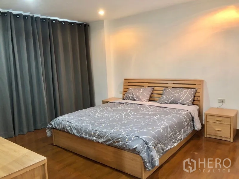 Condominium for rent or sale in Watthana, Bangkok - Spacious bedroom featuring a wooden king bed, gray bedding, bedside tables, and blackout curtains.