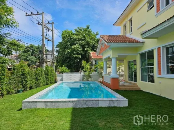 Detached House for rent in Thanyaburi, Pathum Thani - Backyard featuring a private rectangular swimming pool, green lawn and a covered terrace with columns.