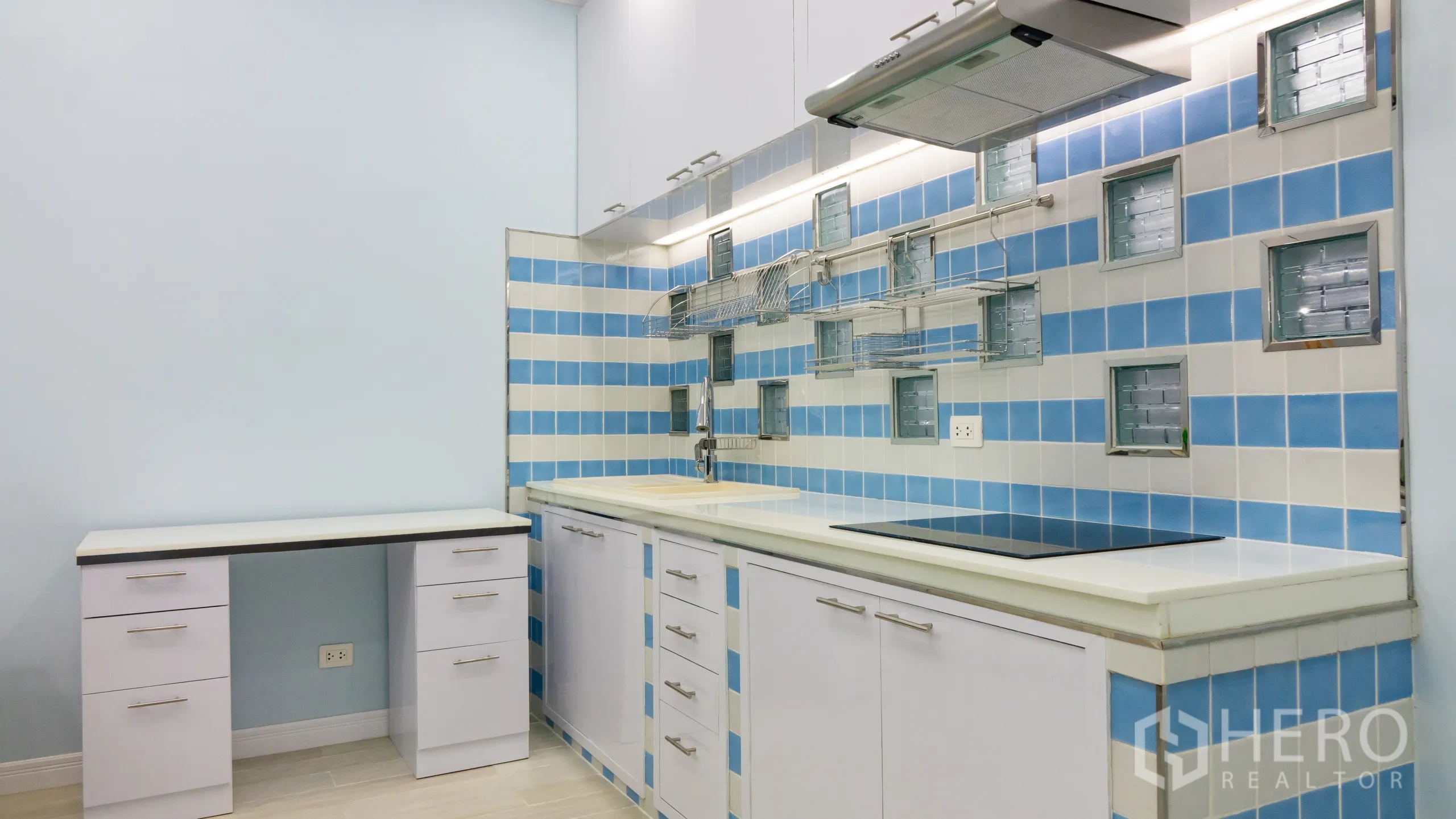 คอนโด for rent or sale in Khlong Toei, Bangkok - ครัวสมัยใหม่ เตาไฟฟ้า เครื่องดูดควัน ฉากหลังกระเบื้องฟ้า‑ขาว