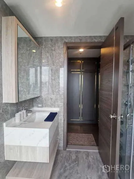 公寓 出售在Huai Khwang, Bangkok - 第二浴室设洗手台、大镜子、灰色石纹瓷砖，并通往更衣区。