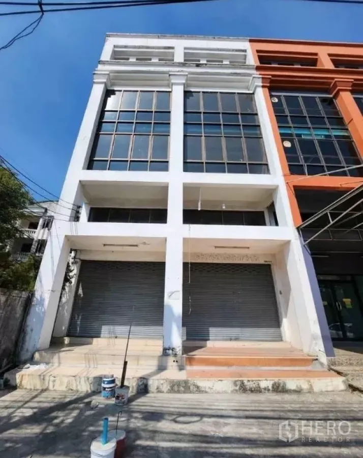 Office Space for rent in Suan Luang, Bangkok - Four-storey commercial office facade with large grid windows and twin roller shutter doors under a blue sky.