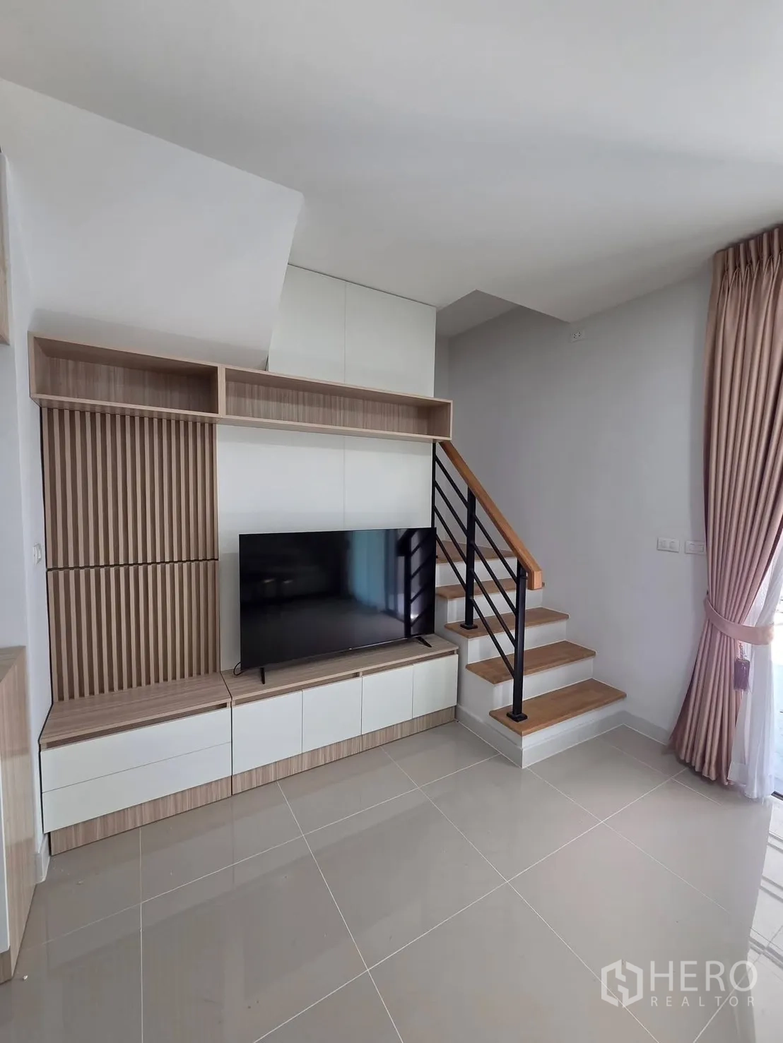 Townhouse for rent in Bang Phli, Samut Prakan - TV console with wood paneling beside a staircase with wooden steps and black railing.