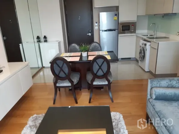 Condominium for rent in Watthana, Bangkok - Dining zone with mirrored wall, elegant chairs, and view toward kitchenette and entry.