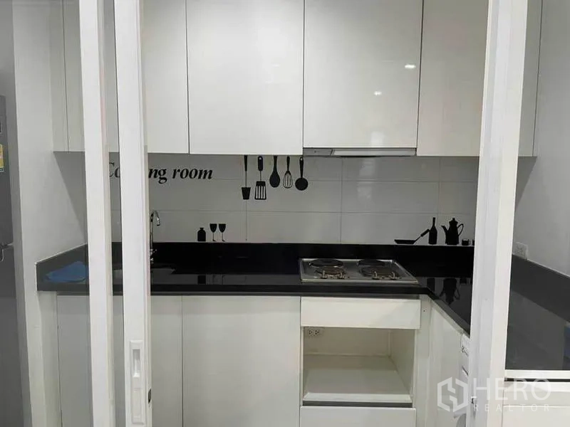 Condominium for rent or sale in Watthana, Bangkok - Compact white kitchen with black countertop, cabinets and two-burner cooktop.