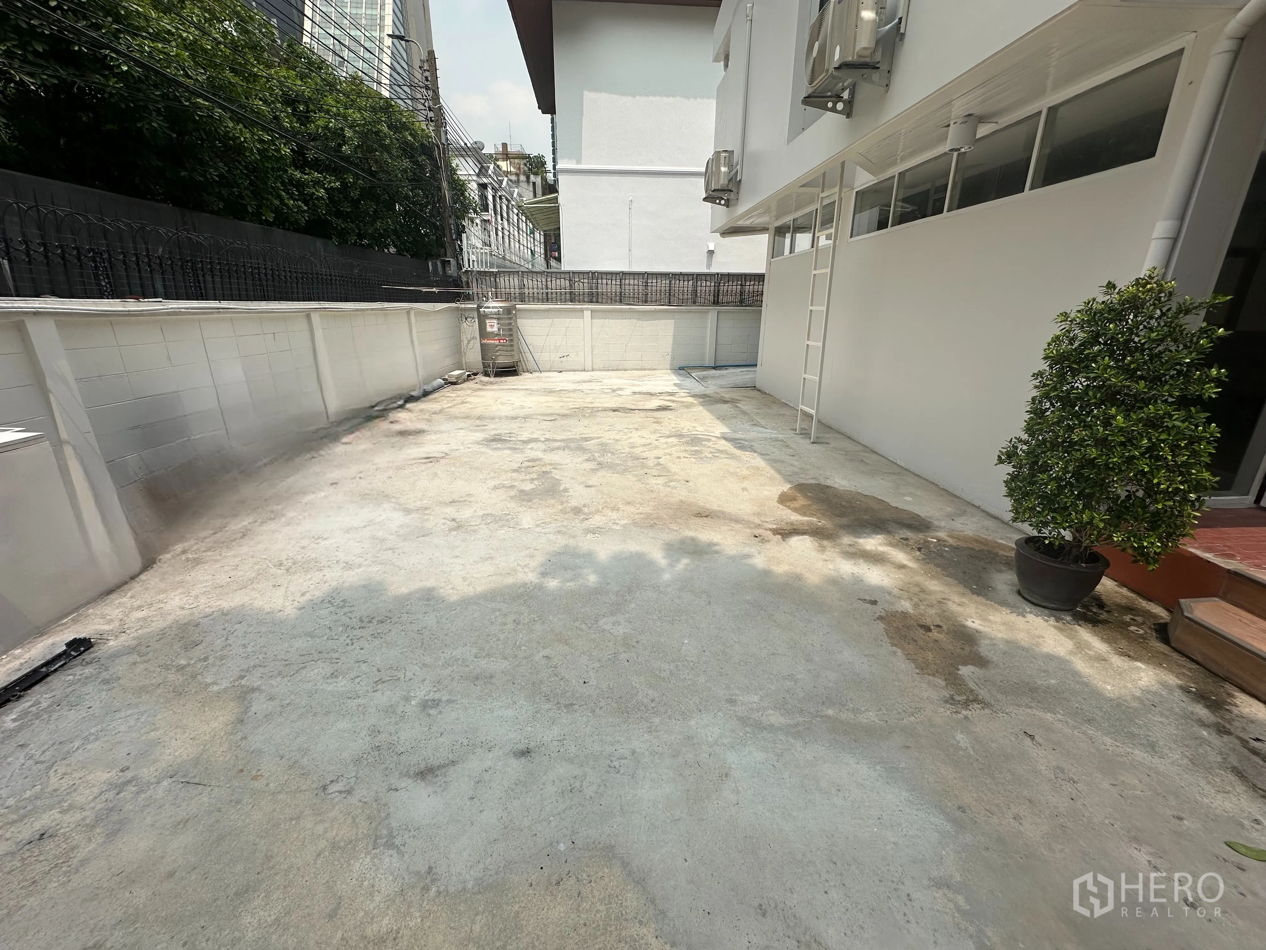 Home Office for rent in Watthana, Bangkok - Wide concrete side yard and driveway beside the building with boundary wall and AC units.
