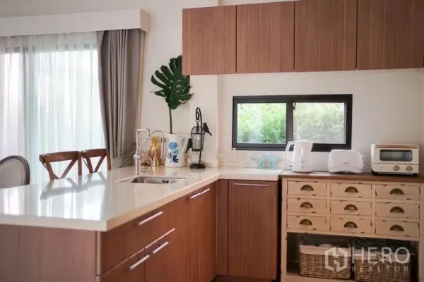 บ้าน ให้เช่าในSai Mai, Bangkok - ครัวรูปตัวแอล ท็อปสีขาว ตู้ไม้ และหน้าต่างมองเห็นสวน
