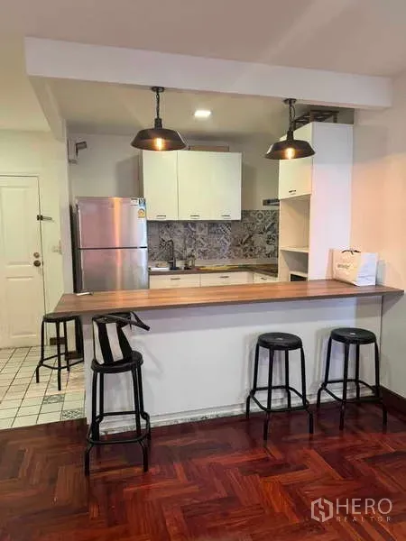 公寓 出租在Sathon, Bangkok - 开放式厨房配吧台、吊灯、不锈钢冰箱与黑色吧椅，位于Supreme Ville。