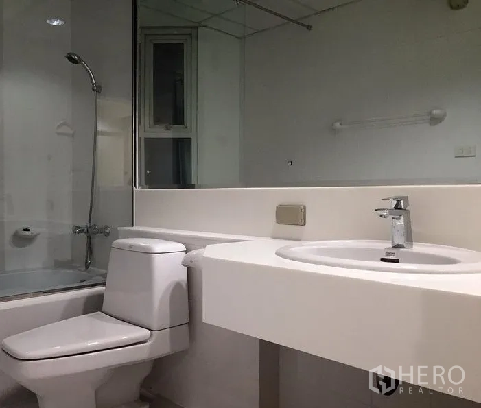 Condominium for rent in Bang Rak, Bangkok - Modern bathroom with bathtub and shower combo, large mirror, toilet and vanity.