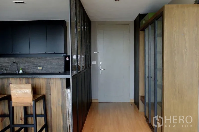 Condominium for sale in Watthana, Bangkok - Entry corridor with wood floors, mesh partition and built-in closets next to the black kitchen.