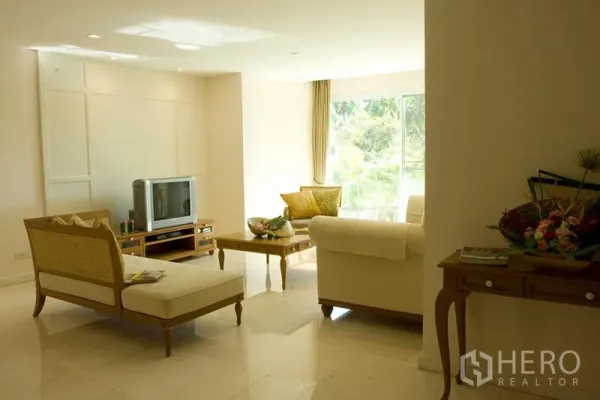 Apartment for rent in Bang Rak, Bangkok - Sunlit living room with sofa set, TV console and coffee table facing a wide window with leafy views.