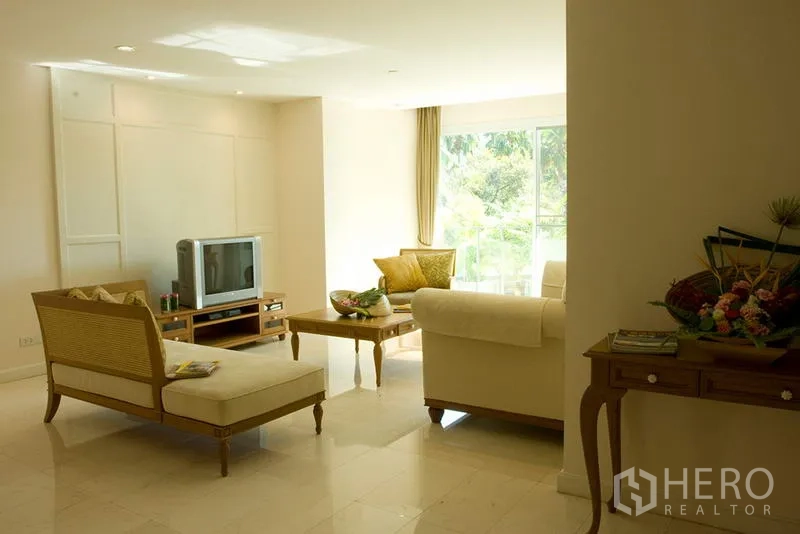 Apartment for rent in Bang Rak, Bangkok - Sunlit living room with sofa set, TV console and coffee table facing a wide window with leafy views.