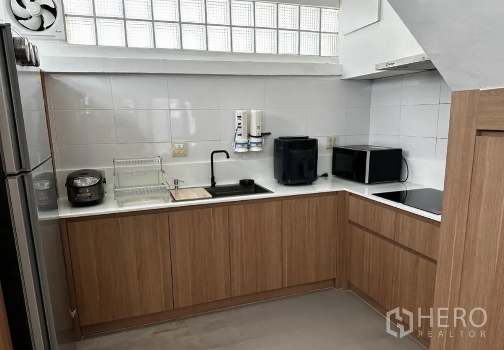 Townhouse for rent in Sathon, Bangkok - Modern L-shaped kitchen with wood cabinets, tile backsplash, and appliances.