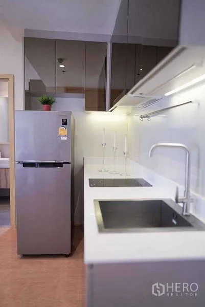 Condominium for rent or sale in Watthana, Bangkok - Galley kitchen close-up showing induction hob, deep sink, and mirrored upper cabinets.