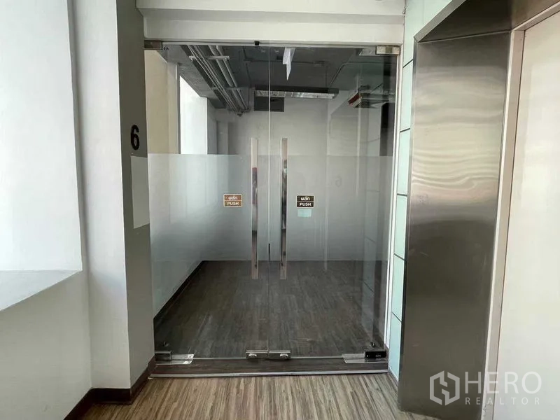 Office Space for rent in Ratchathewi, Bangkok - Glass double-door entrance to the office floor beside a lift with wood-look flooring.