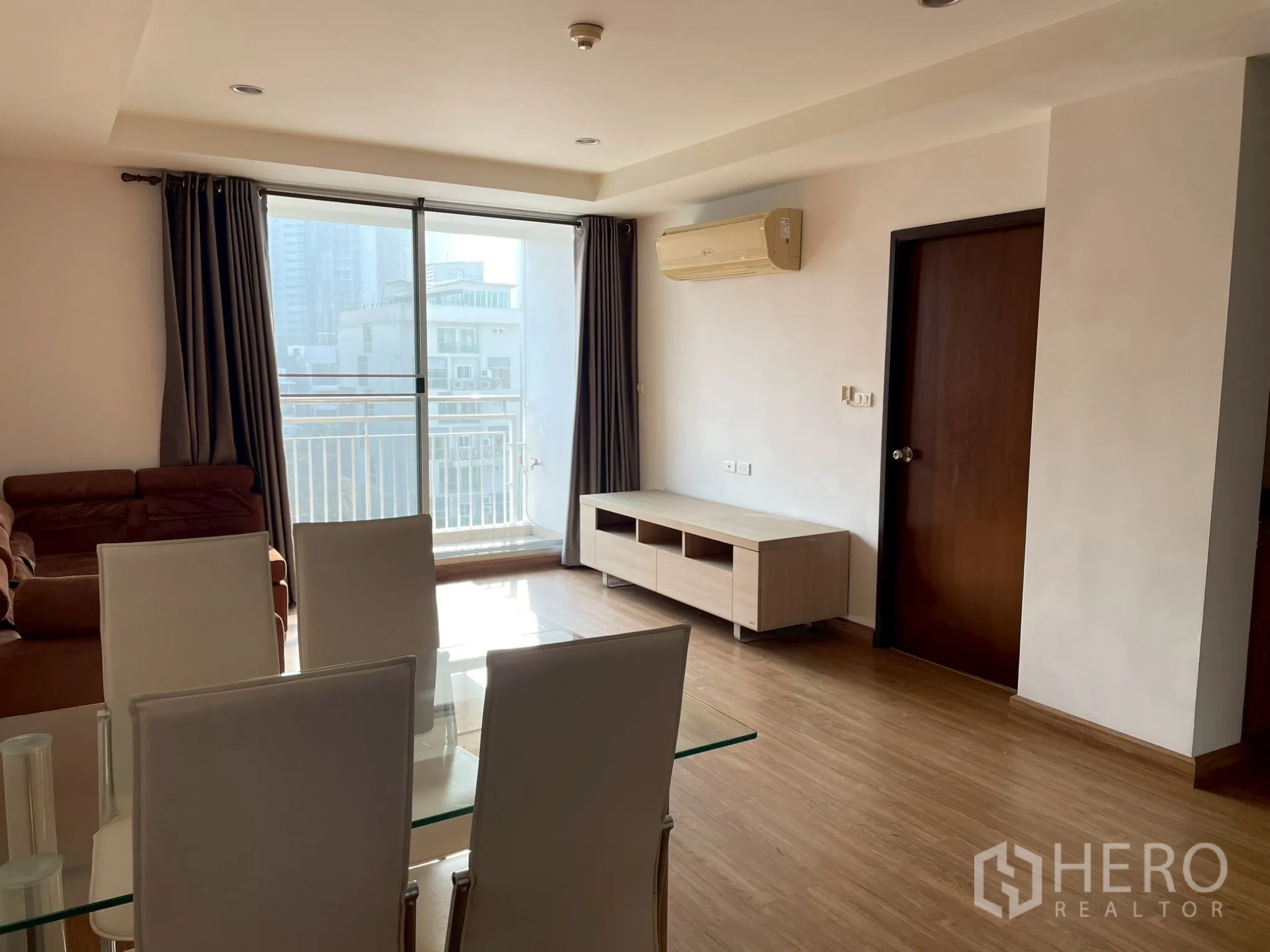Apartment for rent in Khlong Toei, Bangkok - Bright living and dining area with glass doors opening to a balcony and city view.