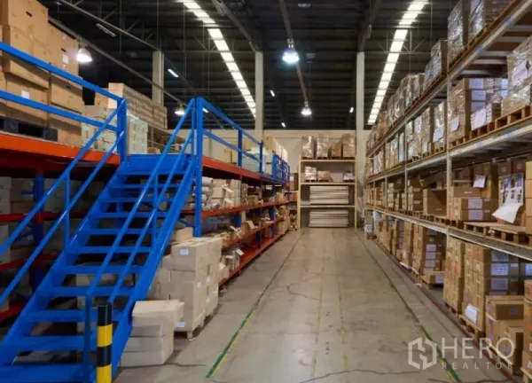 Warehouse for rent in Bang Na, Bangkok - Aisle between tall pallet racks with blue metal staircase and polished concrete flooring.