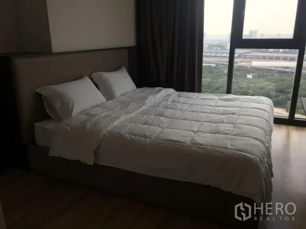 Condominium for rent in Chatuchak, Bangkok - Bedroom with large window, blackout curtains and park-side city view.