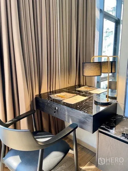 Condominium for rent in Watthana, Bangkok - Compact study nook with black marble desk, chair, and lamp by a curtained window.