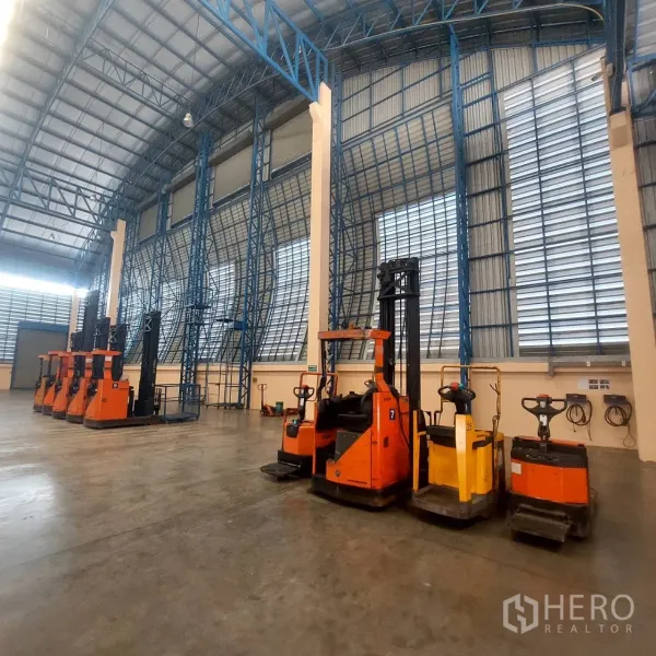 货栈 出租在Mueang Pathum Thani, Pathum Thani - 仓库内多台电动叉车与托盘车停放在高钢架墙下。