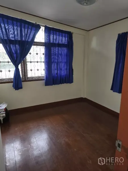 Home Office for rent in Wang Thonglang, Bangkok - Compact bedroom with polished wood flooring, barred windows and blue curtains.